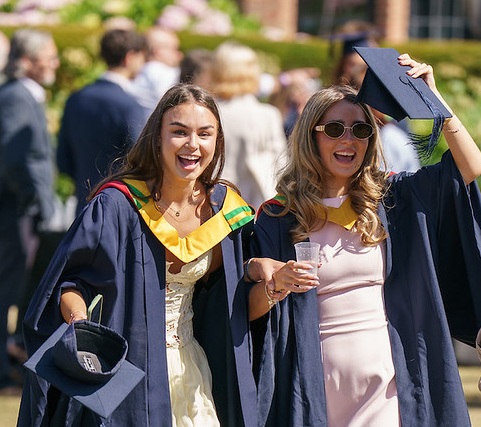 two students walking across rectors lawn in gowns